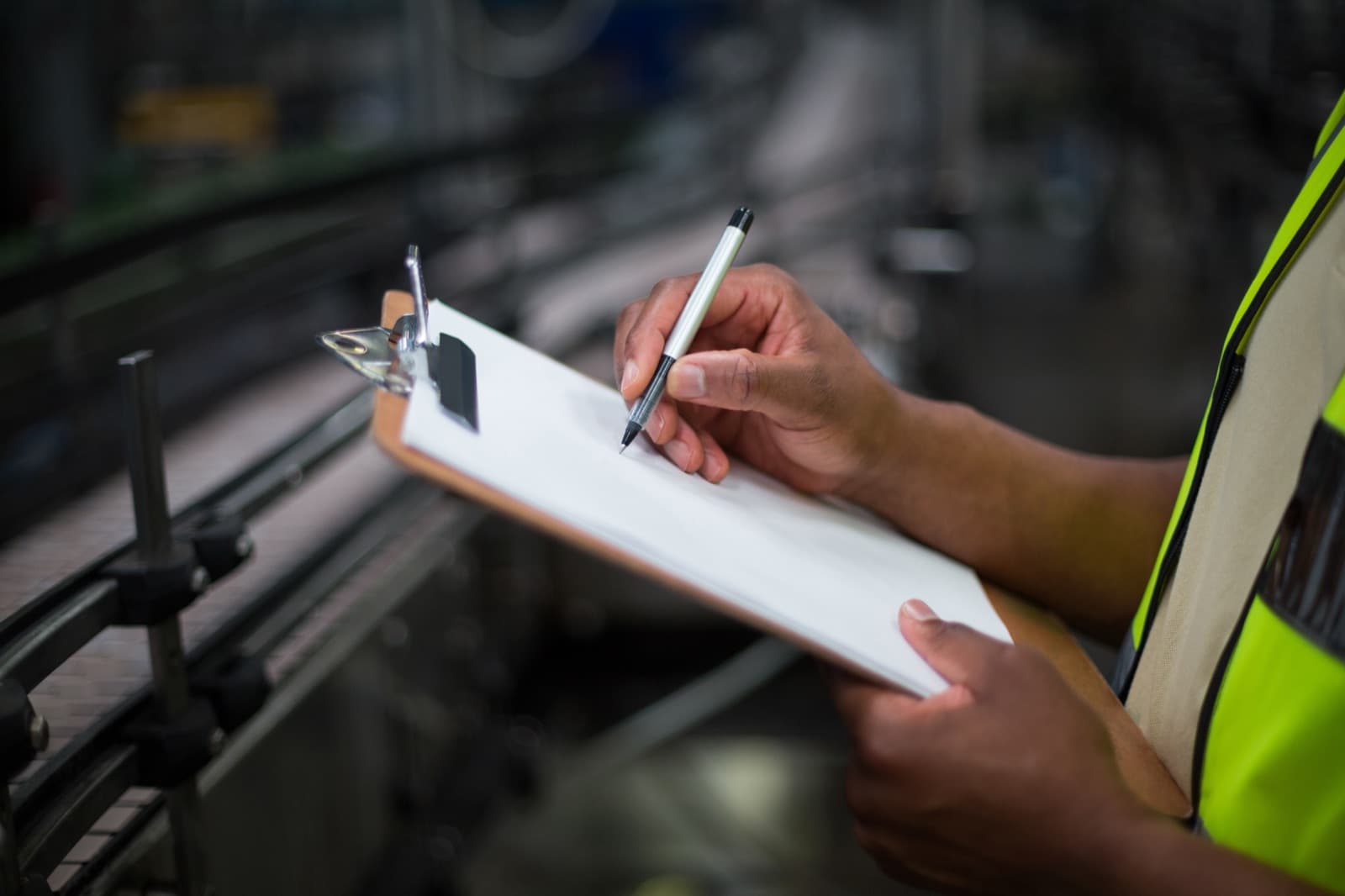 Worker in a high-visibility vest writing on a clipboard during a facility inspection